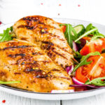 Grilled chicken breast. Fried chicken fillet and fresh vegetable salad of tomatoes, cucumbers and arugula leaves. Chicken meat salad. Healthy food. White background